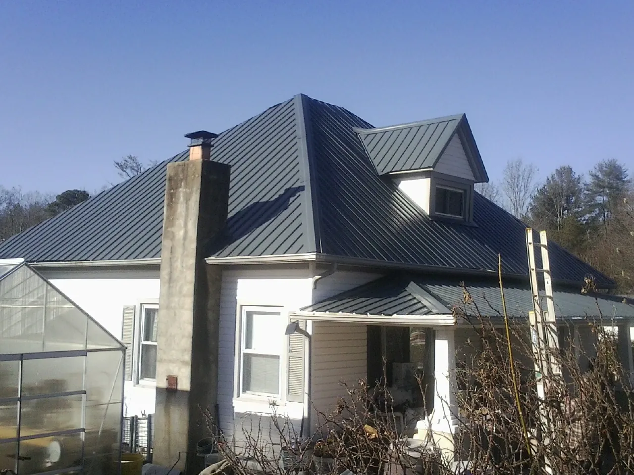 Dark blue standing seam metal roof on a white farmhouse with dormer — Slate & Tile Roof Repair by Roofing Brothers in Wantagh