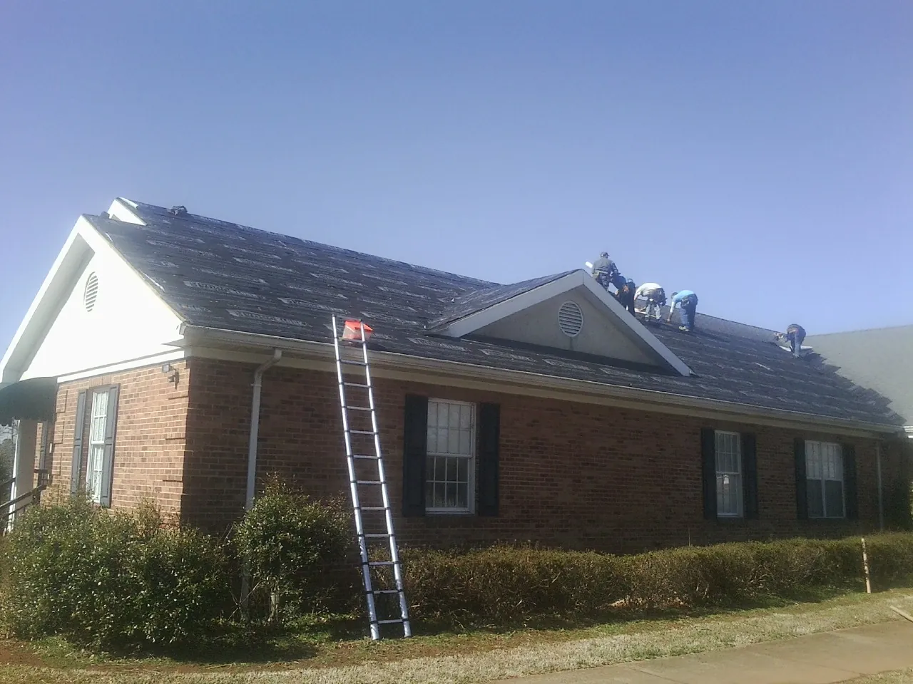 Crew tearing shingles off a brick ranch roof with a ladder set — Emergency Roof Repair work by our crew in Wantagh