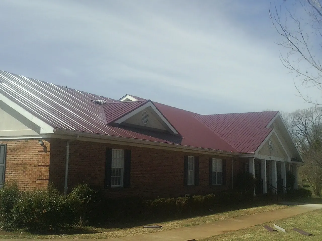 Red metal roof with gabled entries on a long brick building, from a Hail Damage Roof Repair job in Wantagh