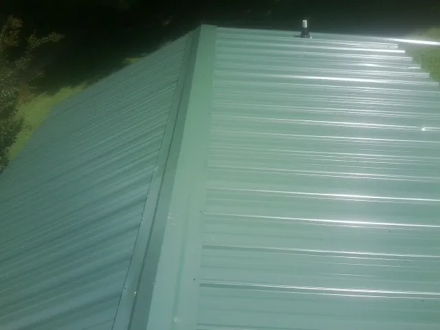 New green metal panels meeting at the ridge of a roof — Flat Roof Repair work by our crew in Wantagh