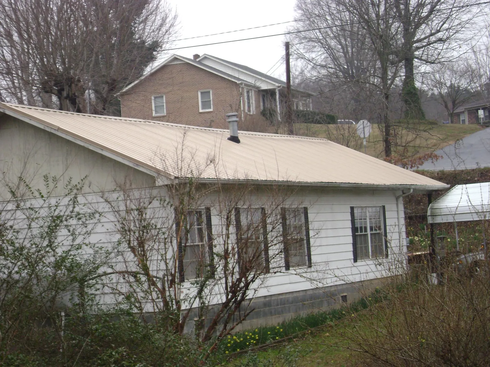 Tan metal roof on a white sided house set into a hillside — Commercial Roofing by Roofing Brothers in Wantagh