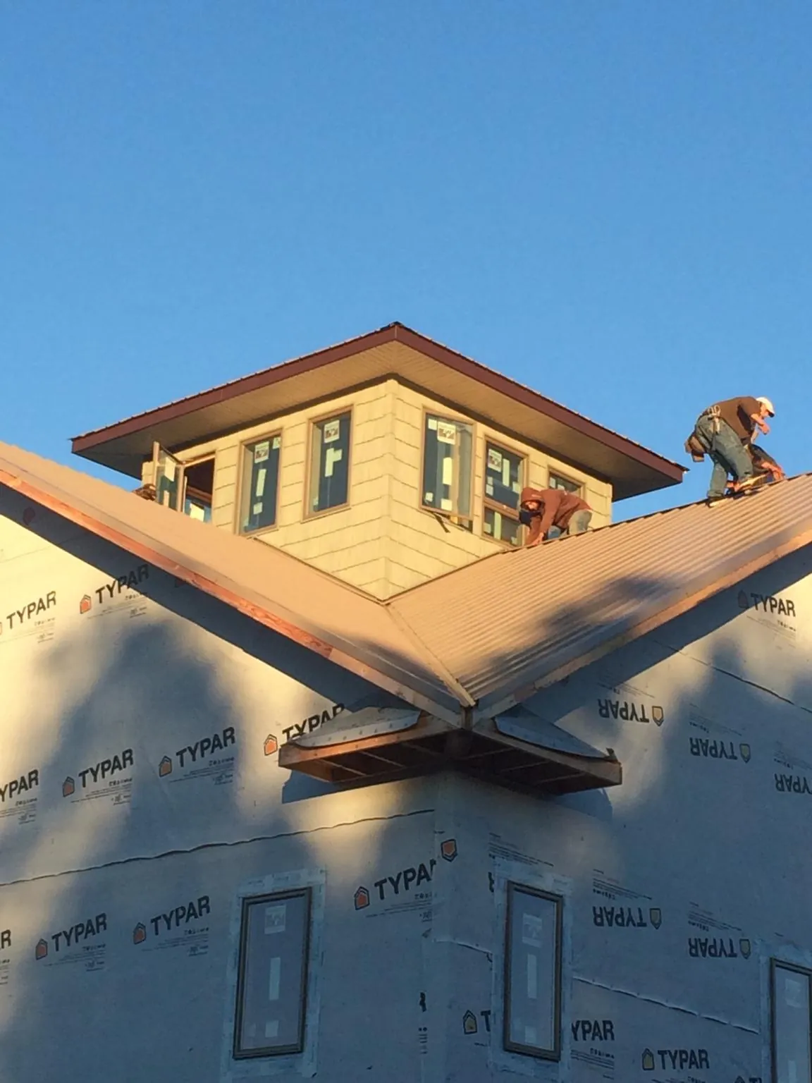 Roofers working around a rooftop cupola on a new metal roof at sunset — Roof Waterproofing in Wantagh by Roofing Brothers
